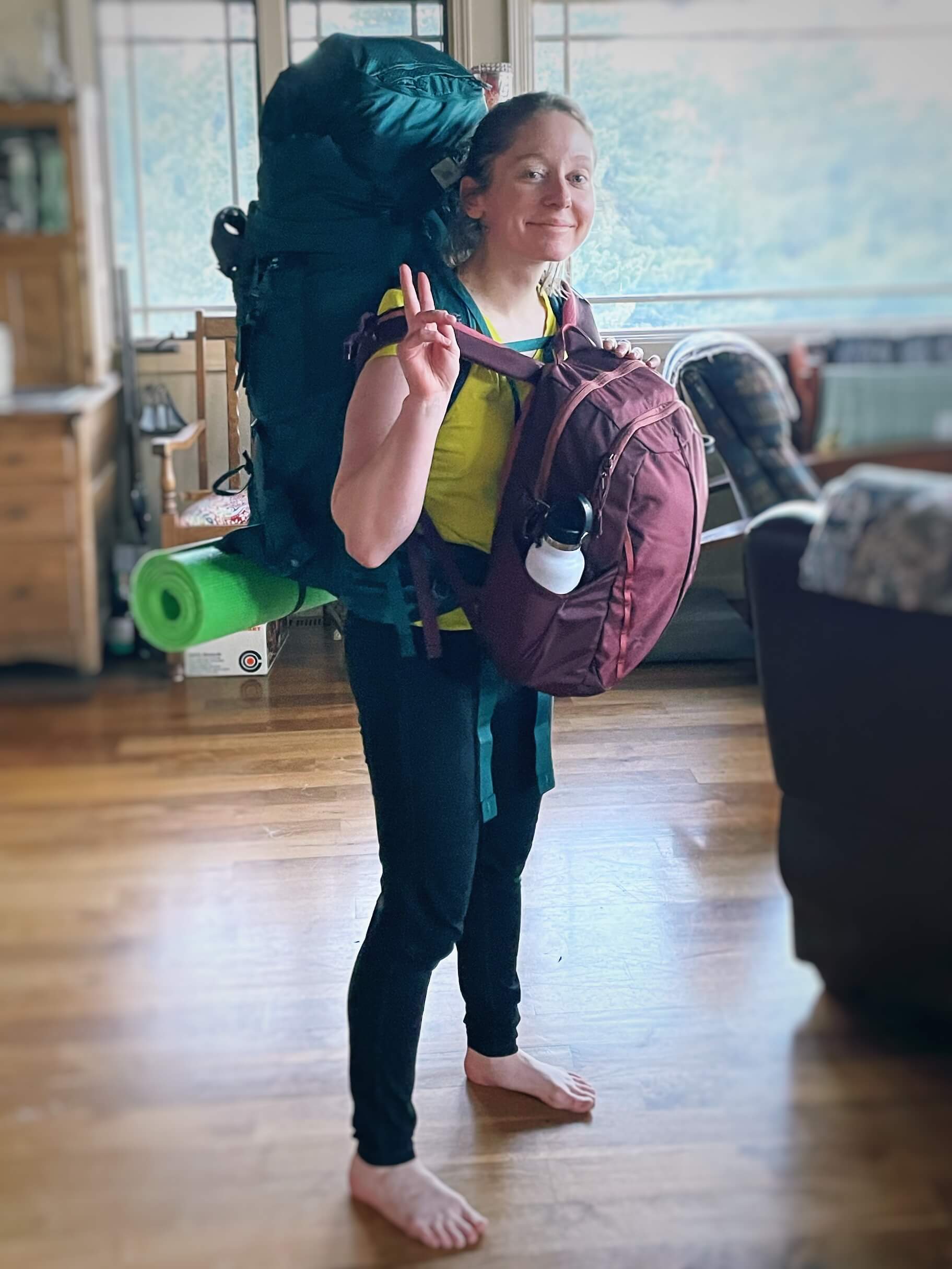 Clara Ritger gives the peace sign to the camera while she wears her backpacking pack on her back and her school backpack on her front.