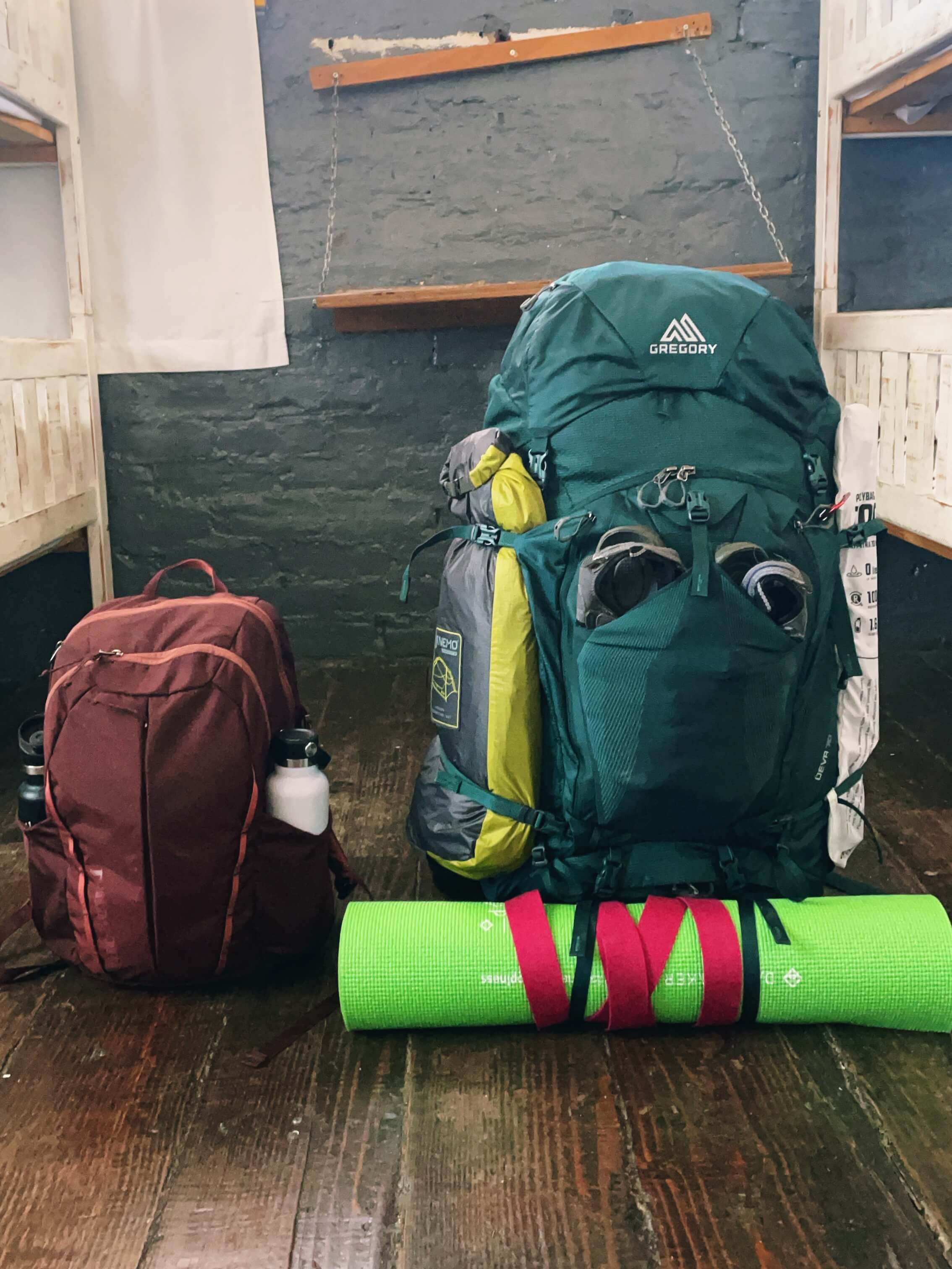 A backpacking pack with a yoga mat and tent strapped to the outside, and a regular backpack.