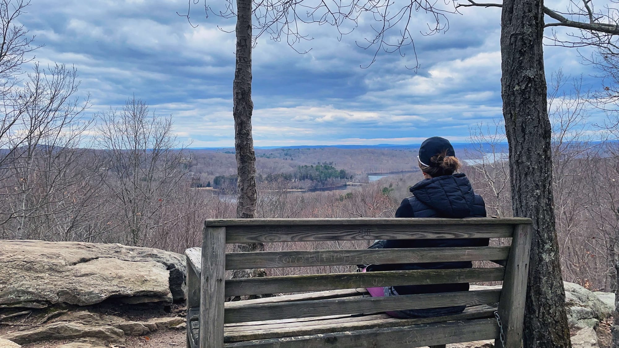 A woman gazes out over upstate New York in the winter. The viewpoint on the hike shows many bare trees.