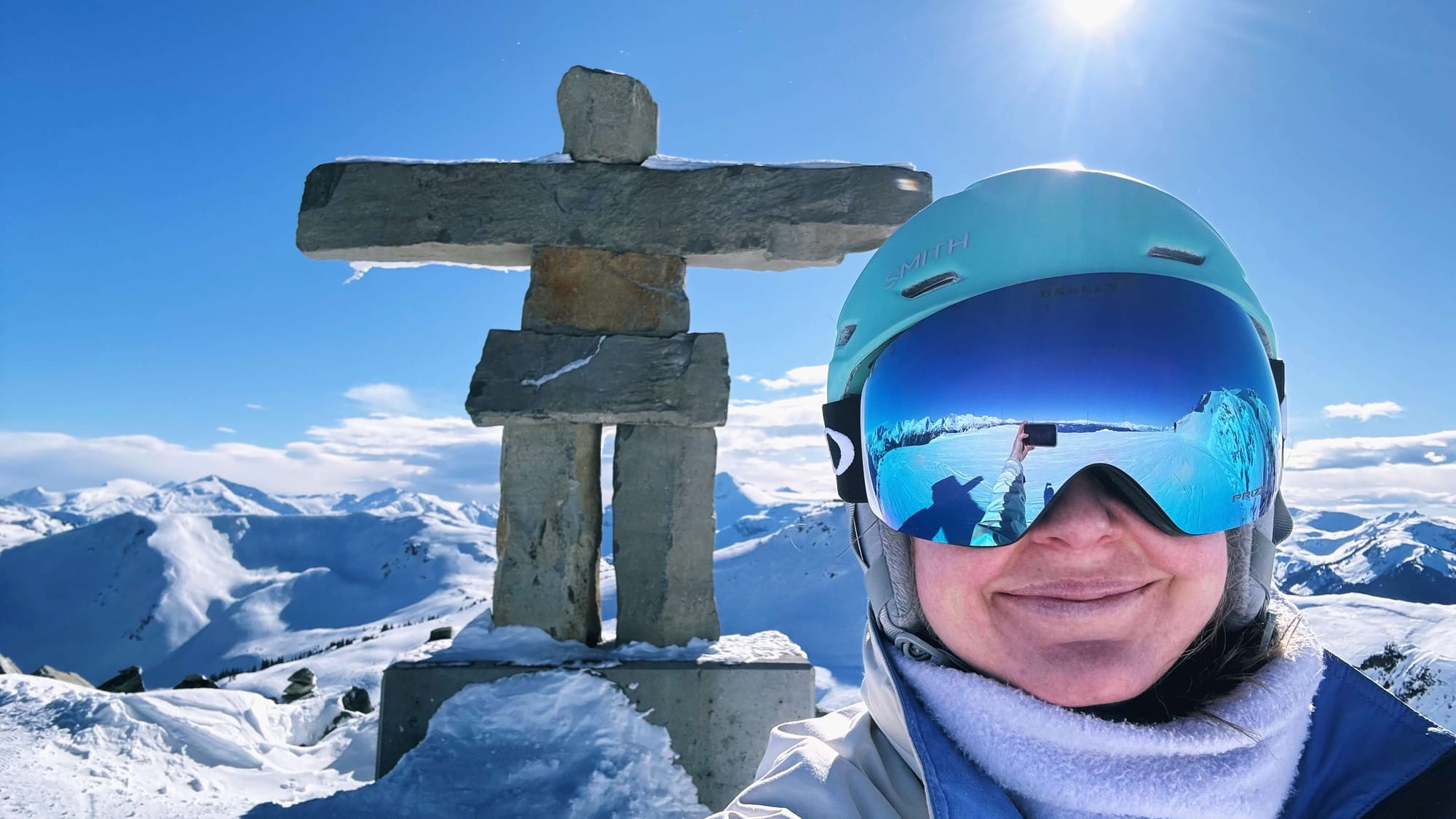 Clara Ritger poses for a selfie in a blue helmet and mirrored goggles, with the Inukshuk stone man.