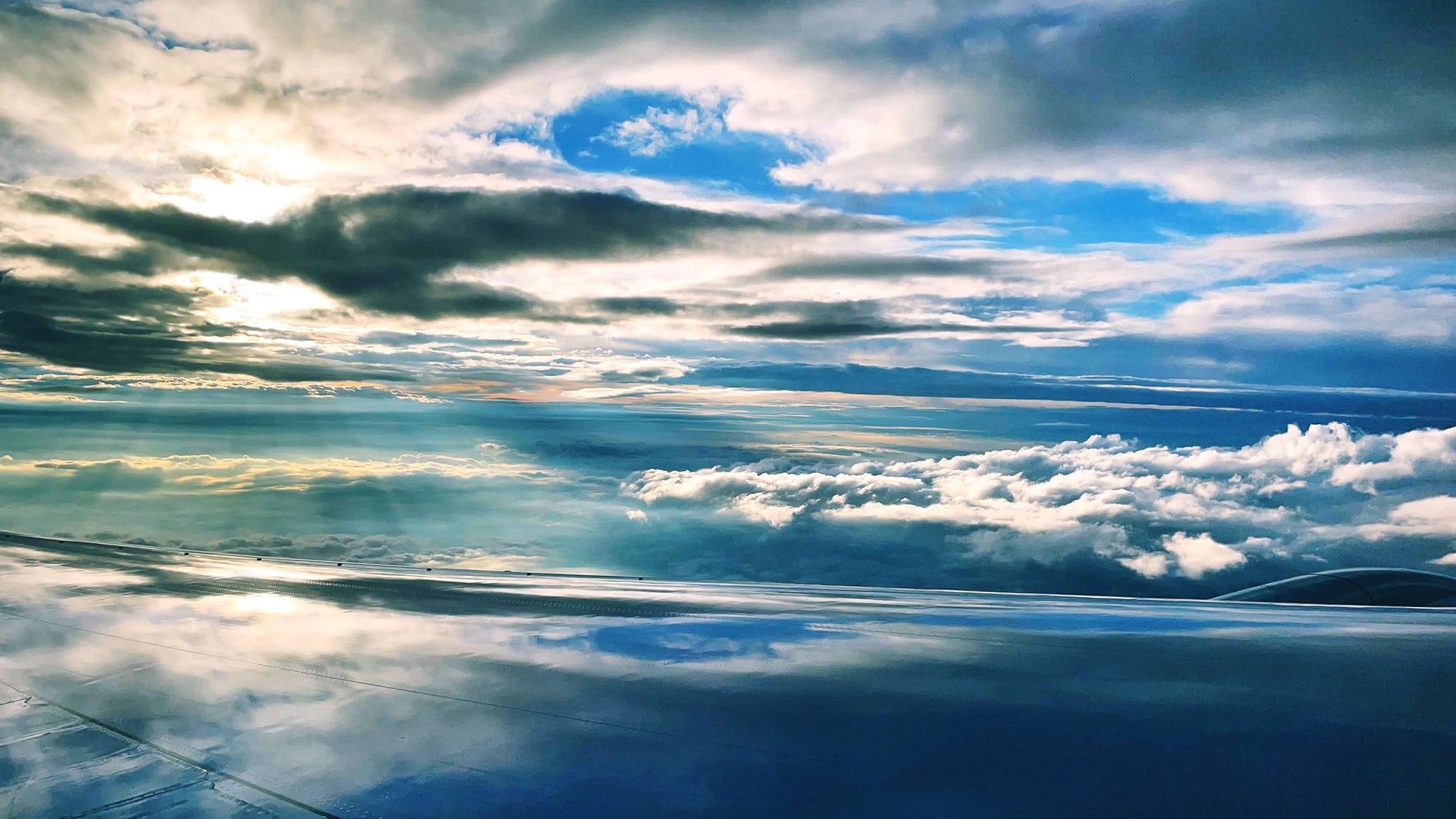 Rays of light shine down. White clouds and blue skies reflect on the plane's wing.