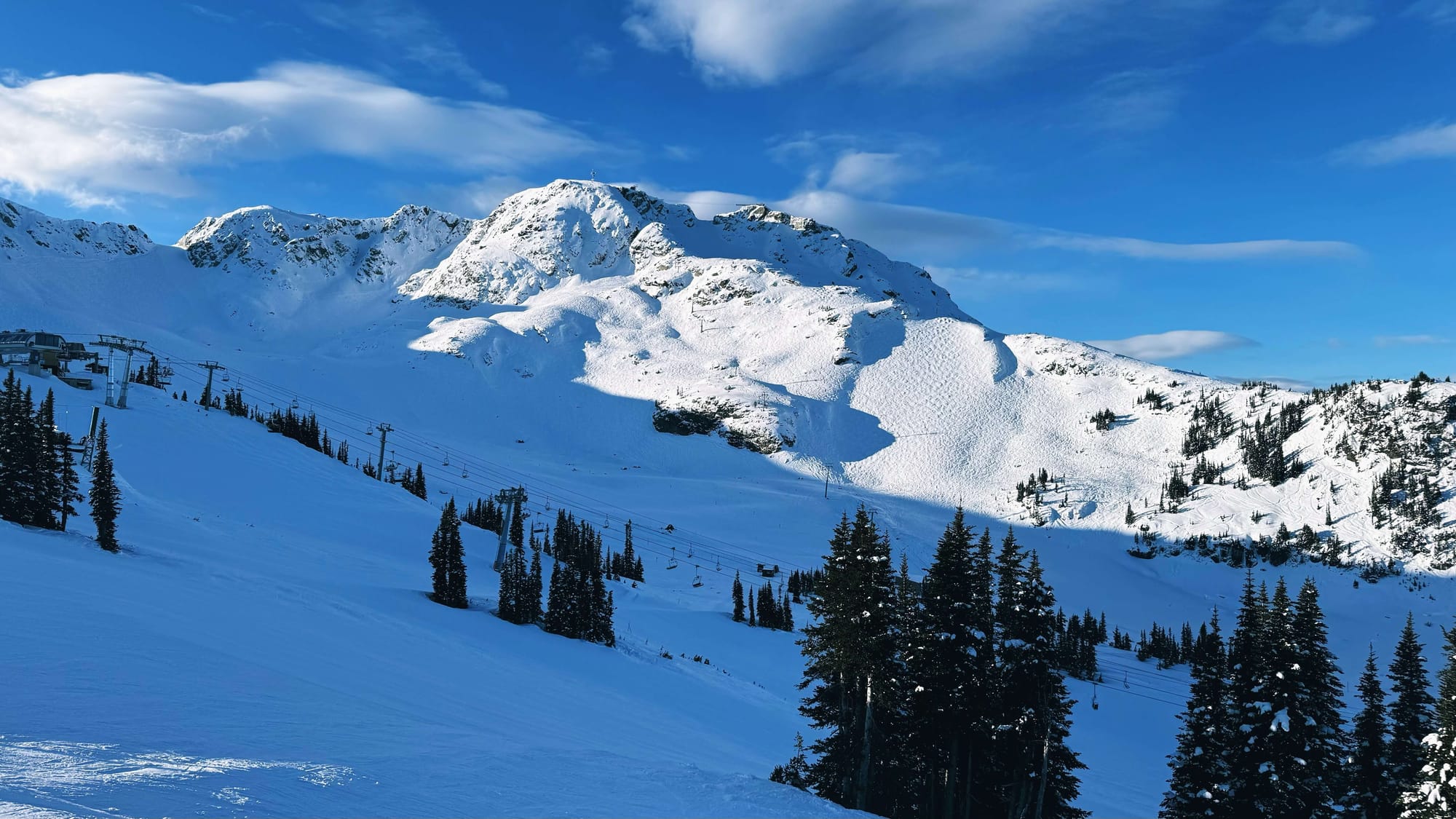 A tall mountain ridgeline and a ski bowl with a ski lift running through the middle.