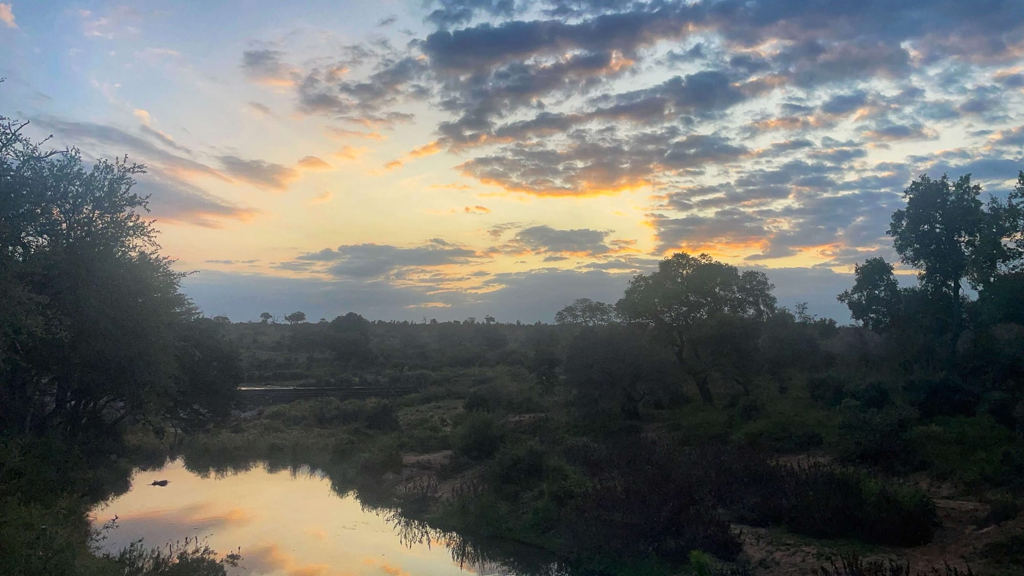 Orange colored sunset clouds reflect in water in Kruger National Park. 