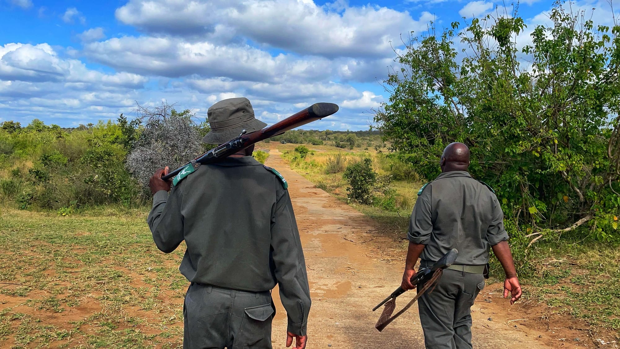 Two Kruger National Park rangers walk on a dirt path with guns.