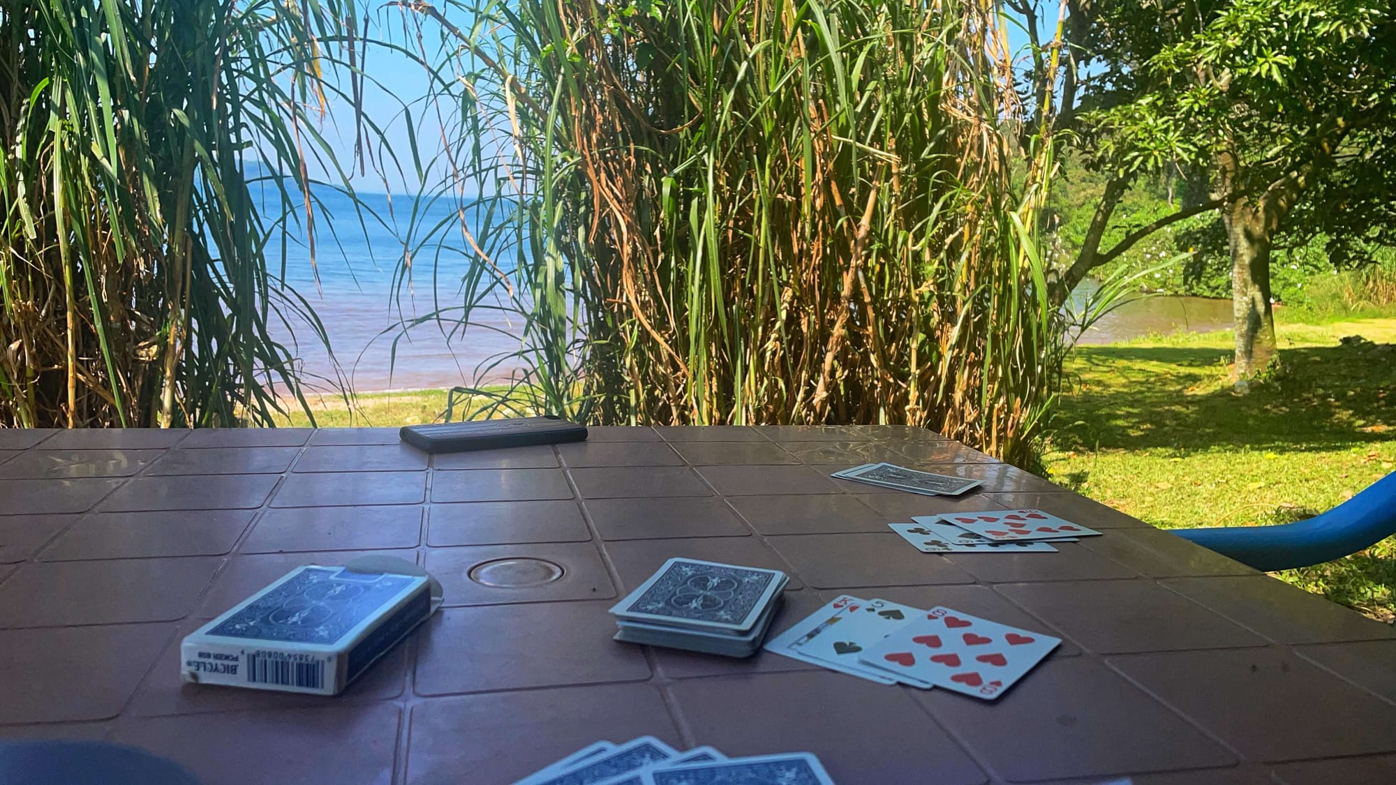 A deck of cards, mid-card game, sit on a plastic table. The lake can be seen in the distance.