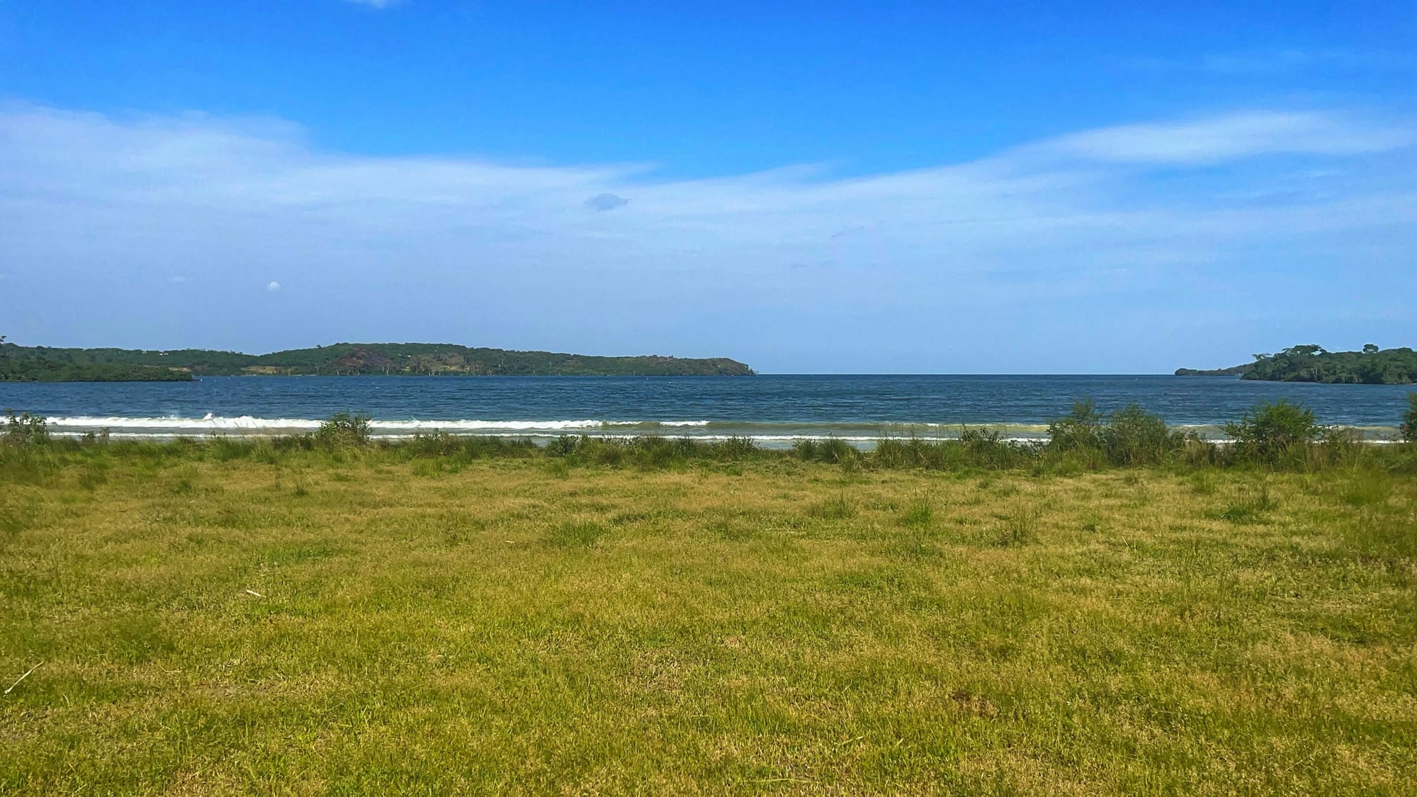 Blue water and white waves break in the distance across a green field.